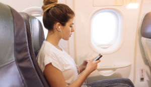 Young woman on airplane choosing music on smartphone